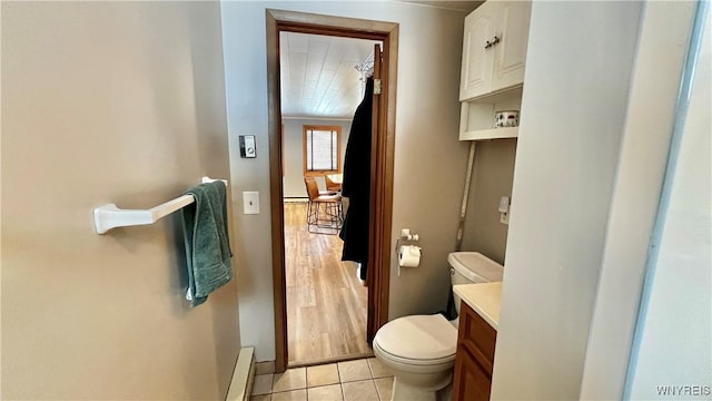 half bath with a baseboard heating unit, tile patterned flooring, vanity, and toilet