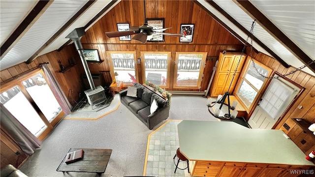 living room with a wood stove, wood walls, ceiling fan, and vaulted ceiling with beams