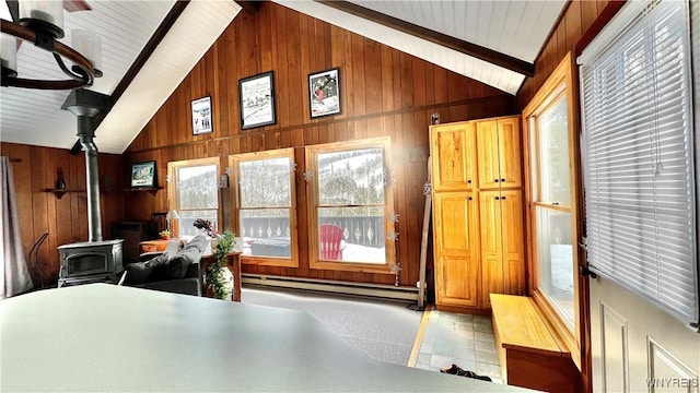 interior space with wooden walls, beamed ceiling, a wood stove, a baseboard heating unit, and high vaulted ceiling