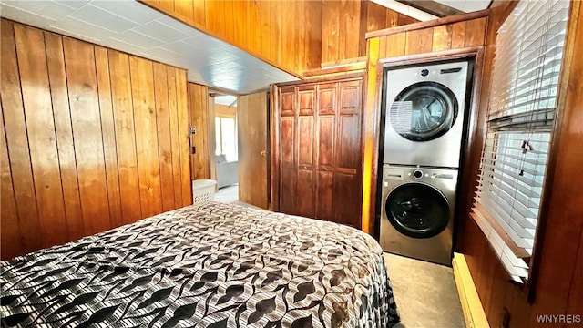 carpeted bedroom with wooden walls and stacked washer / drying machine