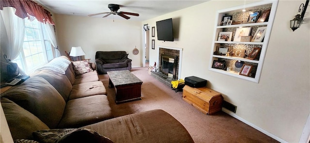 living area with built in features, a ceiling fan, a glass covered fireplace, carpet flooring, and baseboards