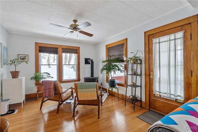 sitting room featuring light wood-style floors, a wood stove, ceiling fan, and baseboards