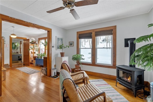 sitting room with a wood stove, light wood finished floors, ceiling fan, and baseboards