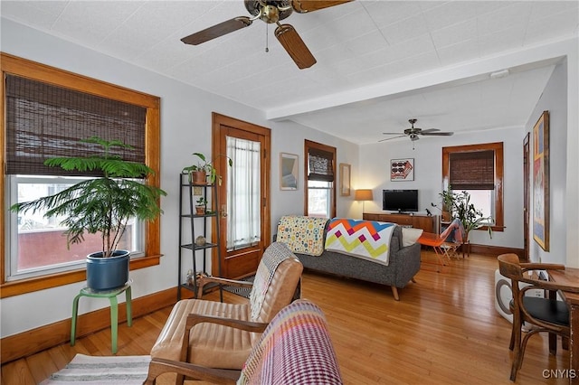 living room featuring a ceiling fan, beam ceiling, baseboards, and wood finished floors