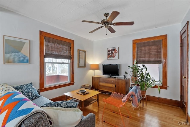 living area with wood finished floors, a ceiling fan, and baseboards