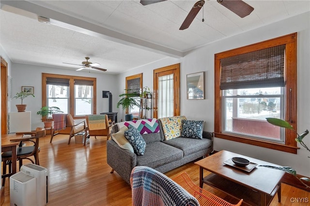 living room with light wood finished floors, a wood stove, and a ceiling fan