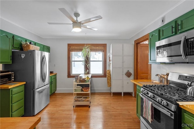 kitchen with appliances with stainless steel finishes, butcher block counters, light wood-style flooring, and green cabinetry