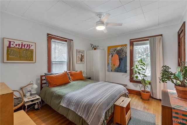 bedroom with multiple windows, ceiling fan, baseboards, and wood finished floors