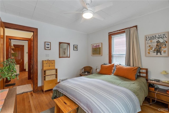 bedroom featuring ceiling fan, light wood-type flooring, visible vents, and crown molding