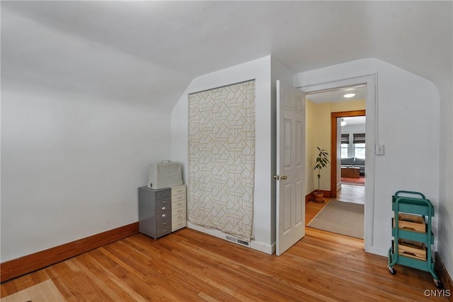 interior space featuring lofted ceiling, light wood-type flooring, visible vents, and baseboards