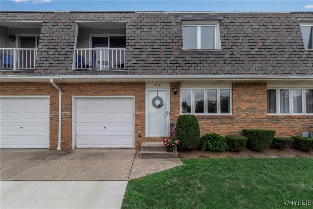 view of property featuring a garage, mansard roof, concrete driveway, and brick siding