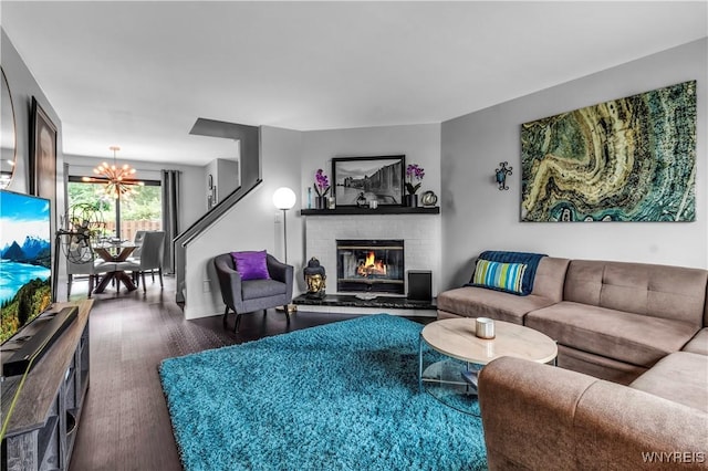 living room with a chandelier, a brick fireplace, and wood finished floors