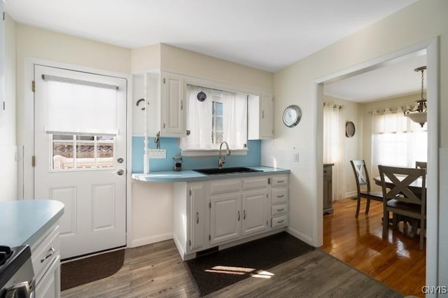 kitchen featuring baseboards, dark wood-style floors, light countertops, white cabinetry, and a sink