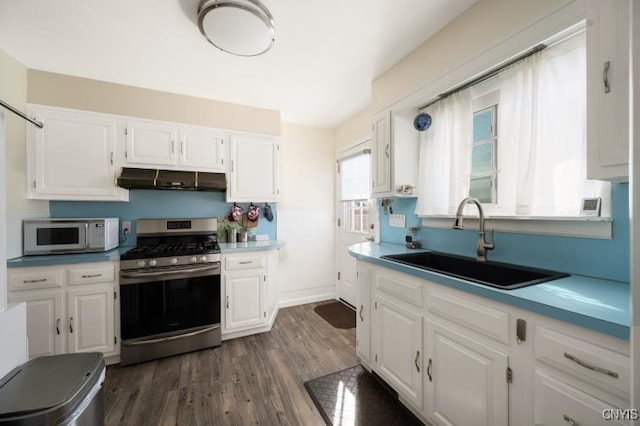 kitchen featuring white microwave, under cabinet range hood, a sink, white cabinetry, and gas stove