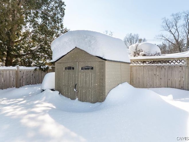 snow covered structure with an outbuilding, a fenced backyard, and a shed