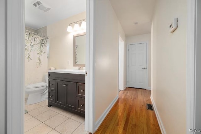 hallway featuring baseboards, visible vents, a sink, and light tile patterned flooring