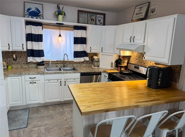 kitchen with butcher block counters, appliances with stainless steel finishes, a peninsula, under cabinet range hood, and a sink