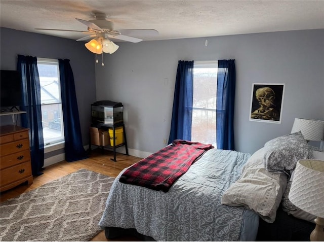 bedroom featuring light wood-type flooring, a textured ceiling, multiple windows, and a ceiling fan