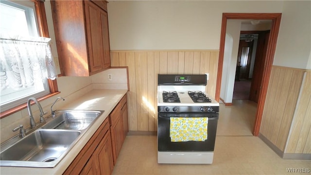 kitchen featuring plenty of natural light, gas range oven, a sink, and wainscoting