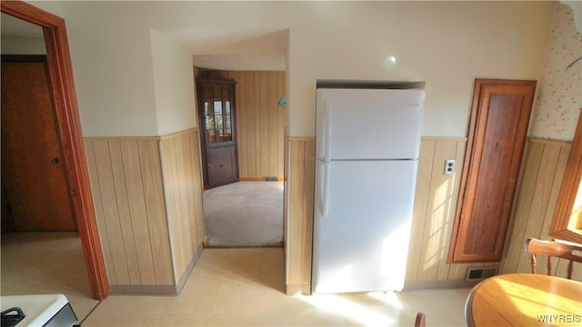 kitchen with freestanding refrigerator, wainscoting, wood walls, and visible vents