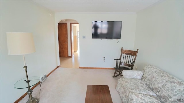 carpeted living area featuring baseboards, arched walkways, and crown molding