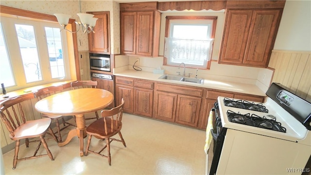 kitchen featuring brown cabinets, white gas stove, stainless steel microwave, a healthy amount of sunlight, and a sink