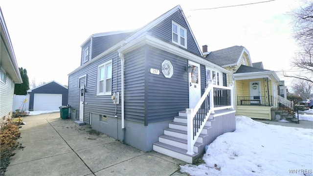 view of front of home with a garage, driveway, a porch, and an outdoor structure