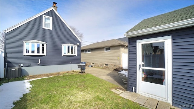 rear view of property with roof with shingles, cooling unit, and a yard