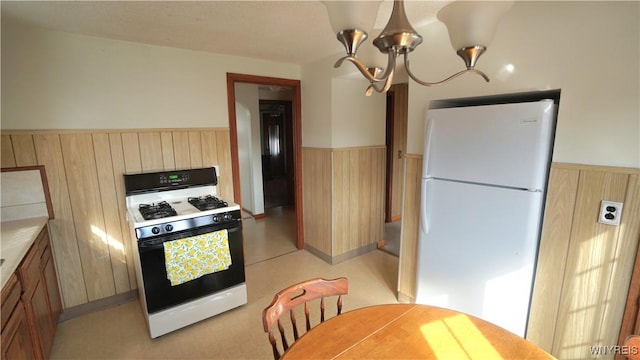 kitchen featuring freestanding refrigerator, gas stove, wainscoting, wood walls, and light brown cabinets