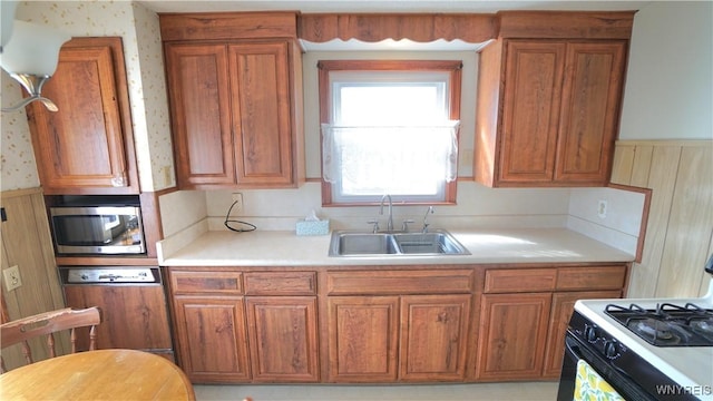 kitchen with brown cabinets, gas range oven, stainless steel microwave, a sink, and dishwasher