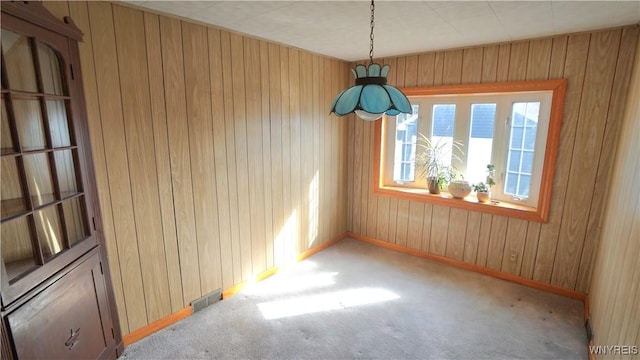 unfurnished room with baseboards, carpet flooring, visible vents, and wooden walls