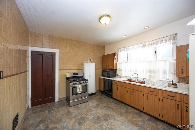 kitchen featuring brown cabinets, tile walls, light countertops, a sink, and black appliances