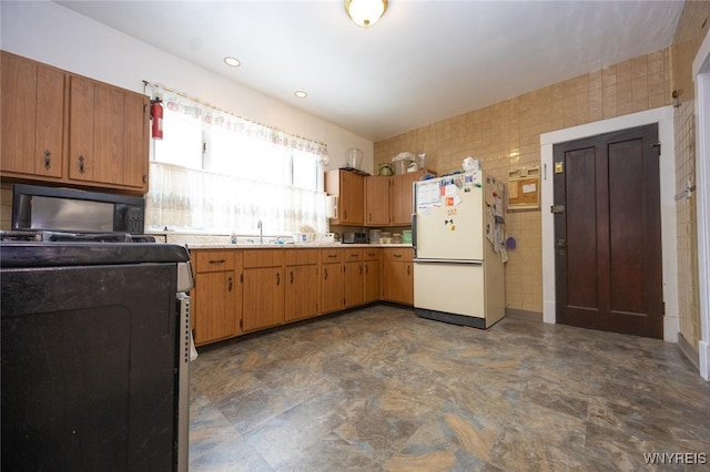 kitchen featuring tile walls, light countertops, brown cabinetry, freestanding refrigerator, and black microwave