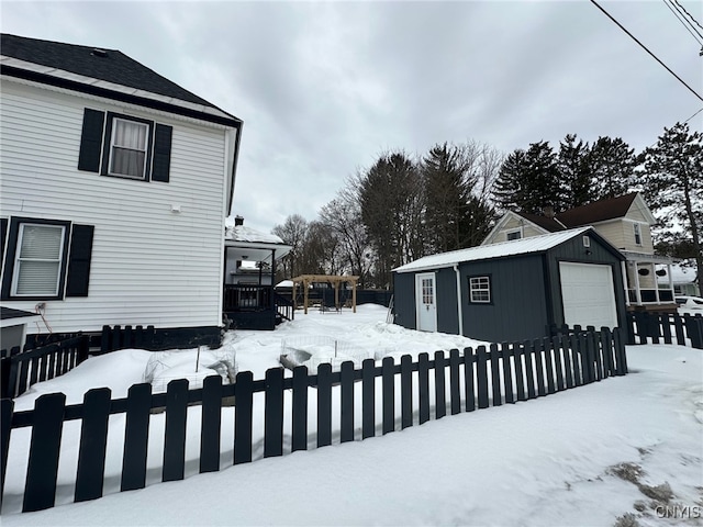 yard covered in snow featuring a garage, an outbuilding, and fence