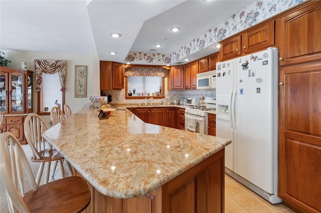 kitchen featuring white appliances, brown cabinets, a peninsula, and a kitchen breakfast bar