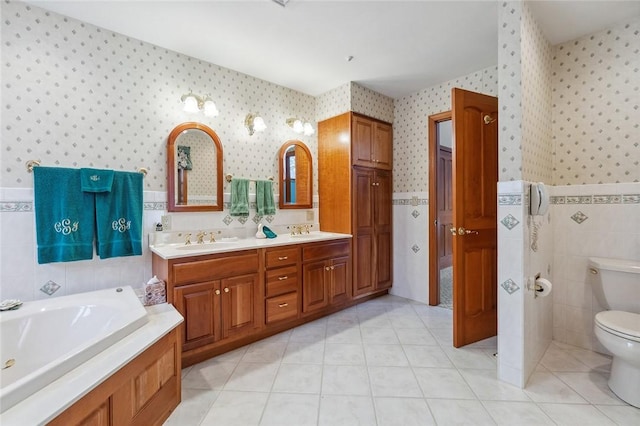 full bathroom with a sink, tile walls, toilet, and wallpapered walls