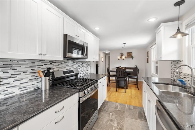 kitchen with decorative light fixtures, stainless steel appliances, backsplash, white cabinets, and a sink