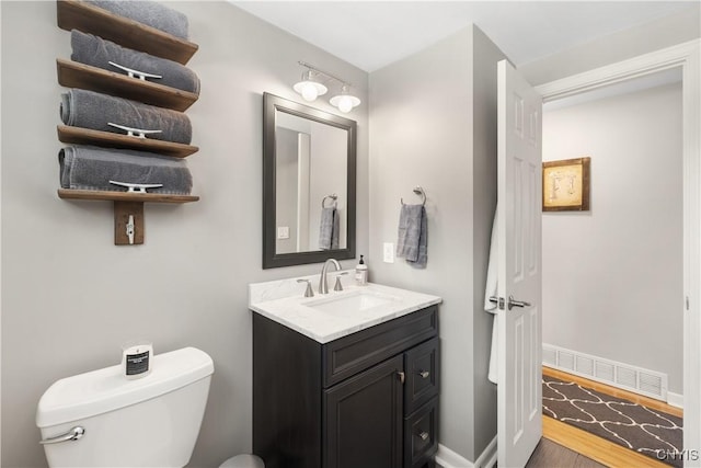 half bath featuring toilet, wood finished floors, vanity, visible vents, and baseboards