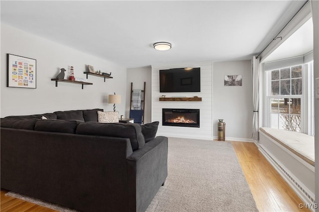 living room with a large fireplace, light wood-style flooring, and baseboards