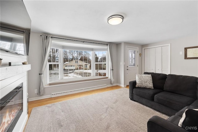 living room featuring plenty of natural light, a baseboard radiator, wood finished floors, and a glass covered fireplace