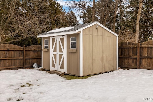 snow covered structure featuring a storage shed, an outdoor structure, and a fenced backyard