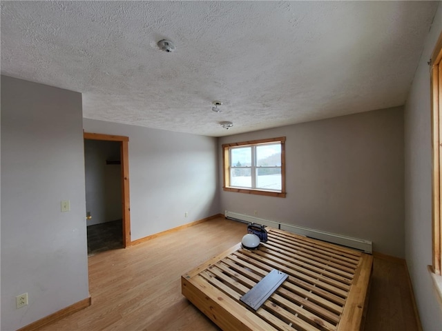 empty room with baseboards, a baseboard heating unit, a textured ceiling, and light wood-style floors