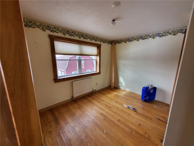 empty room featuring radiator heating unit, baseboards, and hardwood / wood-style floors