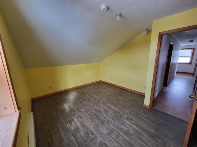 additional living space with a baseboard heating unit, vaulted ceiling, baseboards, and dark wood finished floors