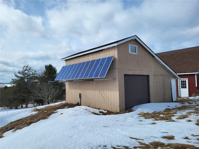 snow covered garage featuring a garage and solar panels