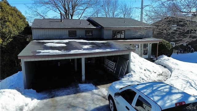 snow covered rear of property featuring a carport and driveway