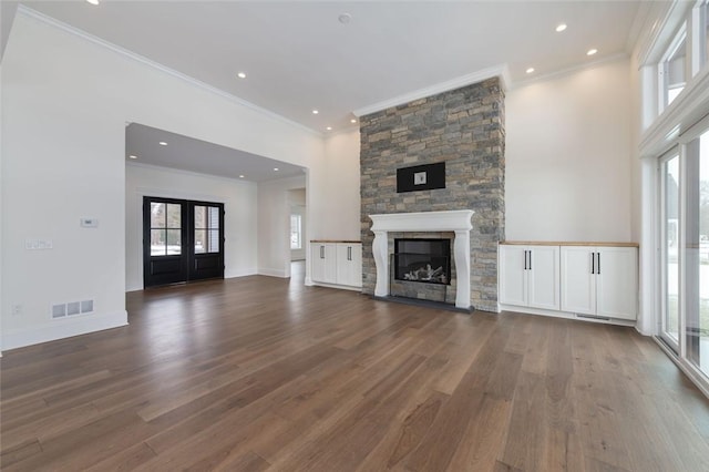 unfurnished living room with a stone fireplace, wood finished floors, visible vents, baseboards, and french doors