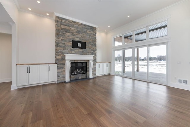 unfurnished living room featuring baseboards, visible vents, wood finished floors, crown molding, and a stone fireplace