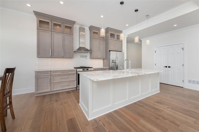 kitchen featuring stainless steel appliances, wall chimney range hood, wood finished floors, and visible vents