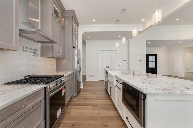 kitchen with light stone counters, stainless steel appliances, light wood-style flooring, a sink, and wall chimney exhaust hood